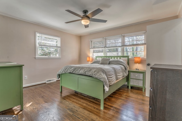 bedroom with ceiling fan, visible vents, baseboards, dark wood finished floors, and crown molding