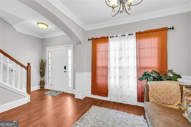 entryway featuring arched walkways, crown molding, stairway, an inviting chandelier, and wood finished floors