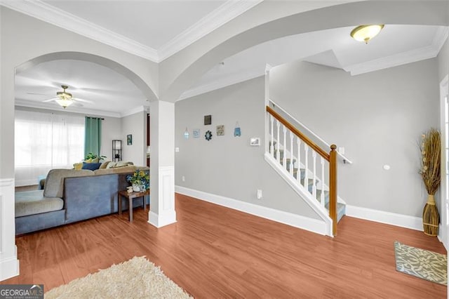 living room featuring arched walkways, wood finished floors, baseboards, stairway, and crown molding