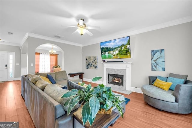 living room with arched walkways, a fireplace, crown molding, visible vents, and light wood-type flooring