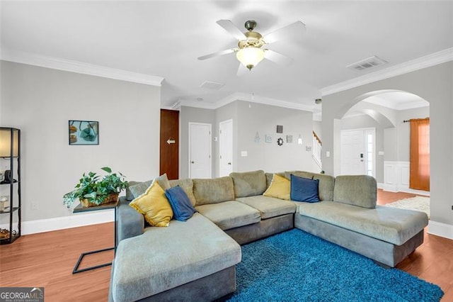 living area featuring arched walkways, crown molding, visible vents, wood finished floors, and baseboards