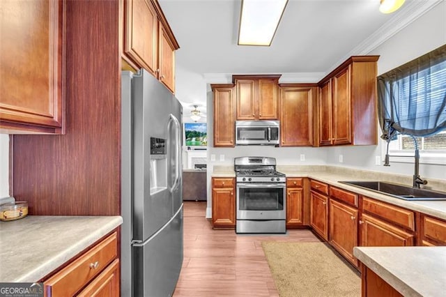 kitchen with light wood finished floors, appliances with stainless steel finishes, ornamental molding, light countertops, and a sink