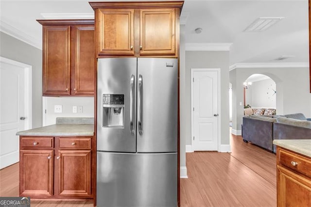 kitchen with arched walkways, visible vents, ornamental molding, light countertops, and stainless steel refrigerator with ice dispenser