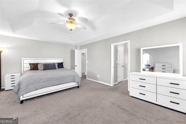 bedroom featuring a ceiling fan, a tray ceiling, light colored carpet, and baseboards