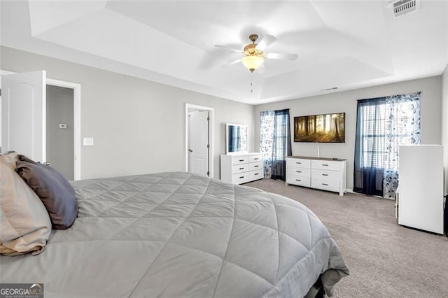 bedroom featuring a tray ceiling, a ceiling fan, visible vents, and light colored carpet