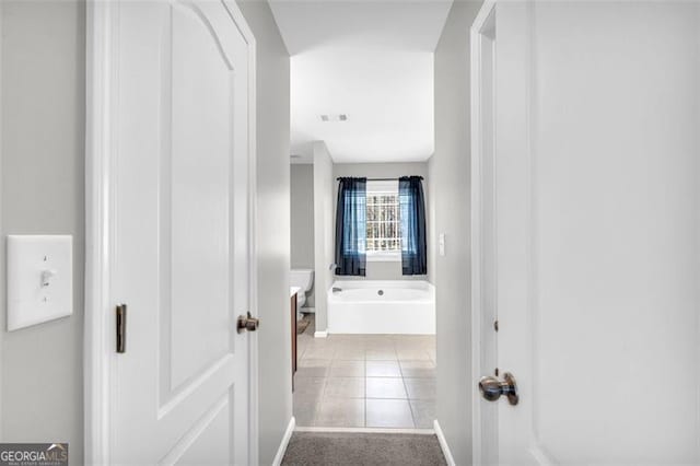 corridor featuring light colored carpet, visible vents, baseboards, and light tile patterned floors