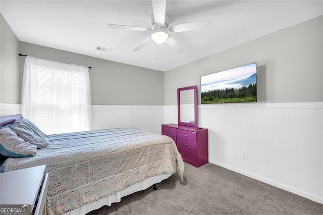 bedroom with carpet floors, a wainscoted wall, visible vents, and ceiling fan