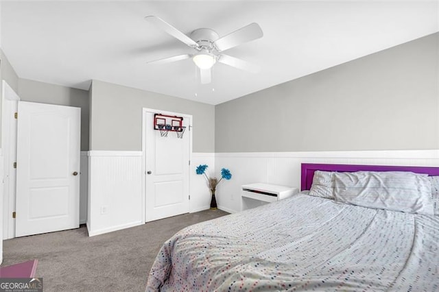 carpeted bedroom featuring a wainscoted wall and a ceiling fan