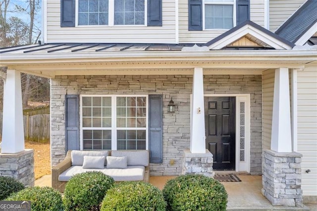 property entrance with stone siding, metal roof, a standing seam roof, covered porch, and fence