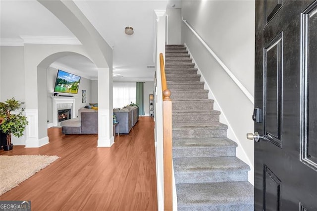 foyer entrance with stairs, crown molding, a lit fireplace, and wood finished floors