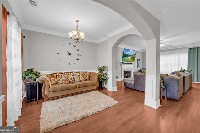 living room with a warm lit fireplace, light wood-style flooring, ornamental molding, and visible vents