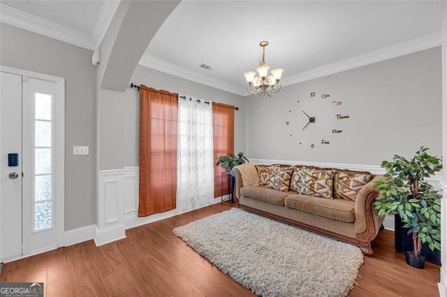 living room featuring crown molding, a notable chandelier, visible vents, wainscoting, and wood finished floors