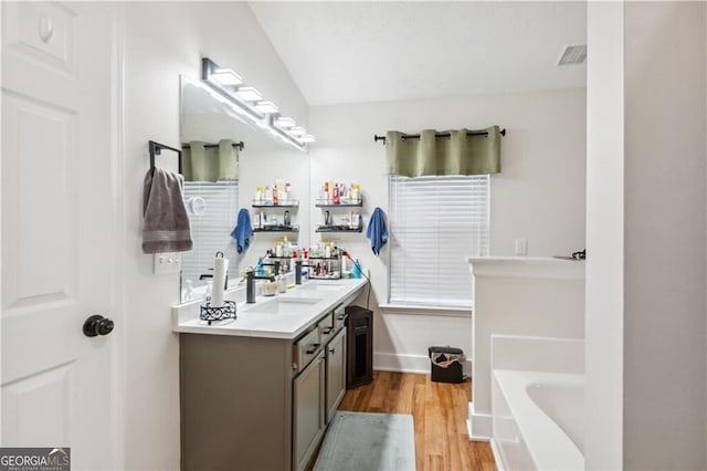 full bathroom featuring double vanity, visible vents, a sink, wood finished floors, and a bath