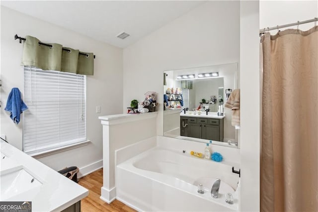 bathroom with a garden tub, visible vents, vanity, wood finished floors, and baseboards