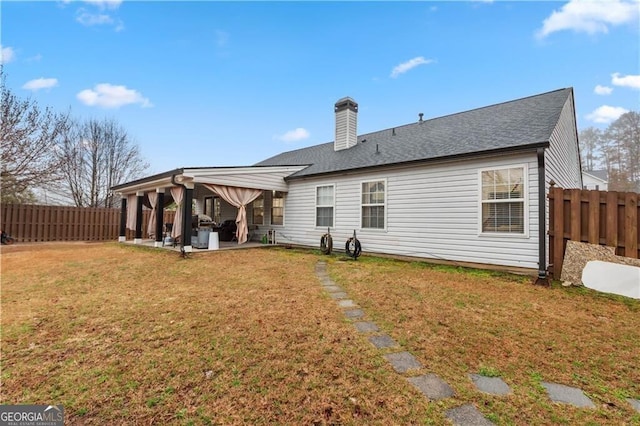 back of property with a shingled roof, a fenced backyard, a chimney, a yard, and a patio area