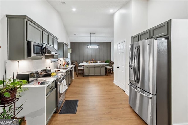 kitchen with decorative light fixtures, stainless steel appliances, gray cabinets, light countertops, and a sink