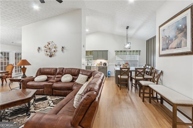 living area with light wood-type flooring, vaulted ceiling, a textured ceiling, and ceiling fan