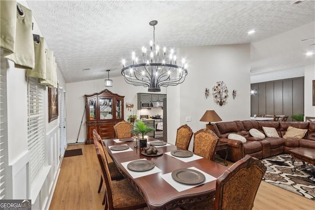 dining space featuring a textured ceiling, a notable chandelier, visible vents, light wood-style floors, and vaulted ceiling