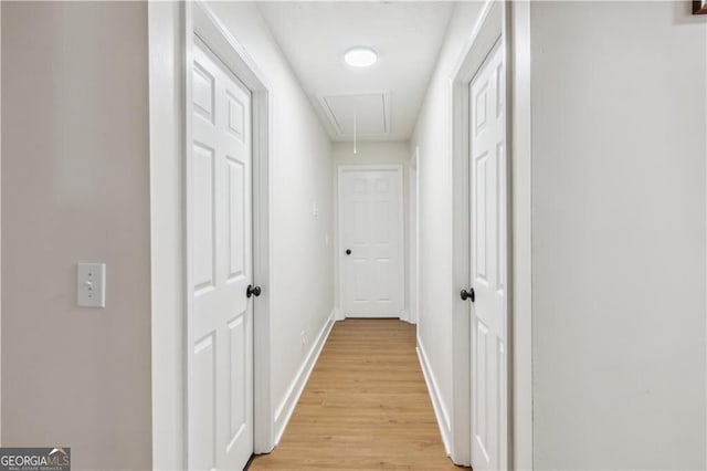 hall with attic access, baseboards, and light wood finished floors