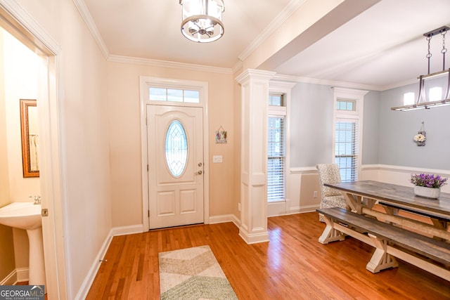 entryway with light wood-style flooring, baseboards, ornamental molding, decorative columns, and an inviting chandelier