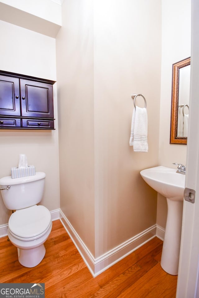 half bath with a sink, toilet, baseboards, and wood finished floors