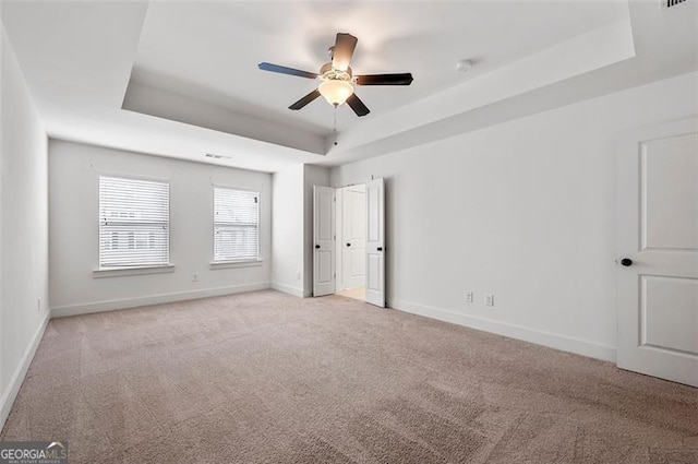 unfurnished bedroom featuring a tray ceiling, light carpet, visible vents, and baseboards