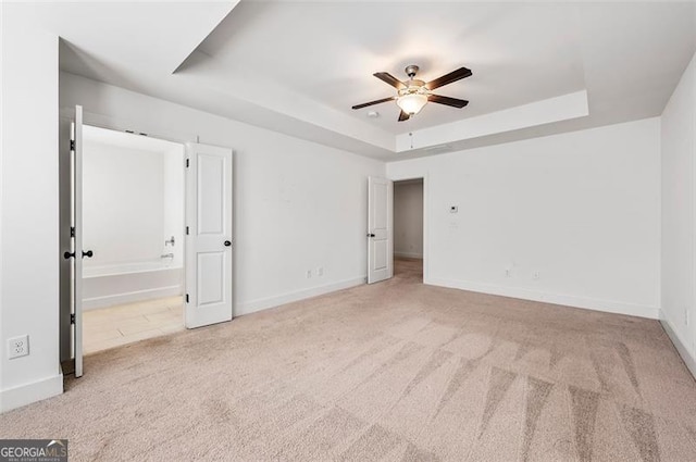 unfurnished bedroom with light carpet, a tray ceiling, and baseboards