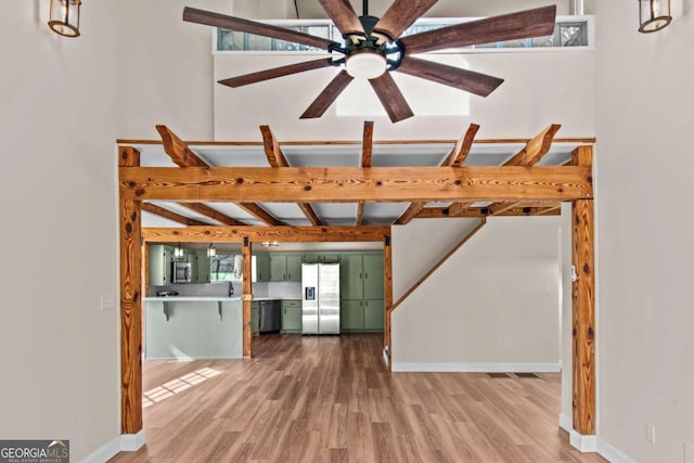 unfurnished living room with ceiling fan, beamed ceiling, wood finished floors, and baseboards