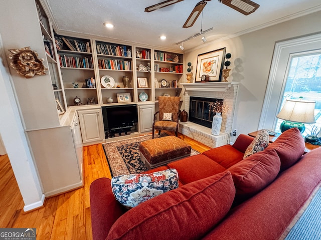 living room featuring ceiling fan, a textured ceiling, a fireplace, light wood-style floors, and ornamental molding