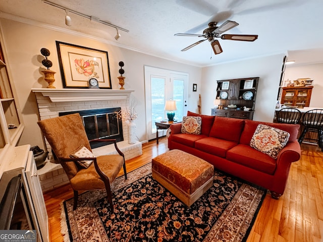 living room featuring a fireplace, wood-type flooring, ornamental molding, a ceiling fan, and a textured ceiling