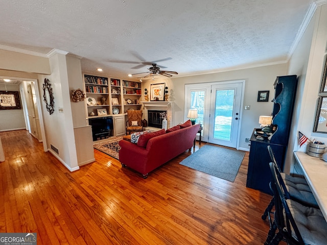 living room with crown molding, a fireplace, a ceiling fan, a textured ceiling, and hardwood / wood-style floors