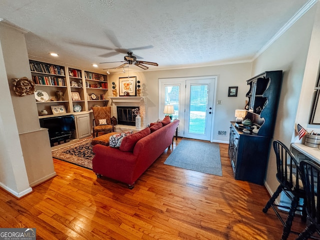 living room with a textured ceiling, baseboards, a brick fireplace, light wood-type flooring, and crown molding