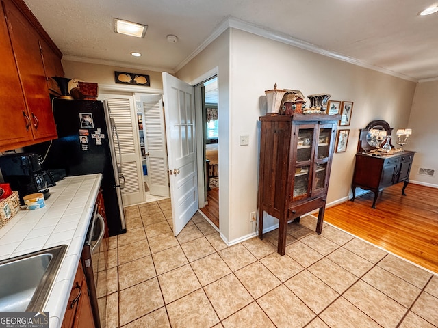 kitchen featuring tile countertops, light tile patterned floors, ornamental molding, and baseboards