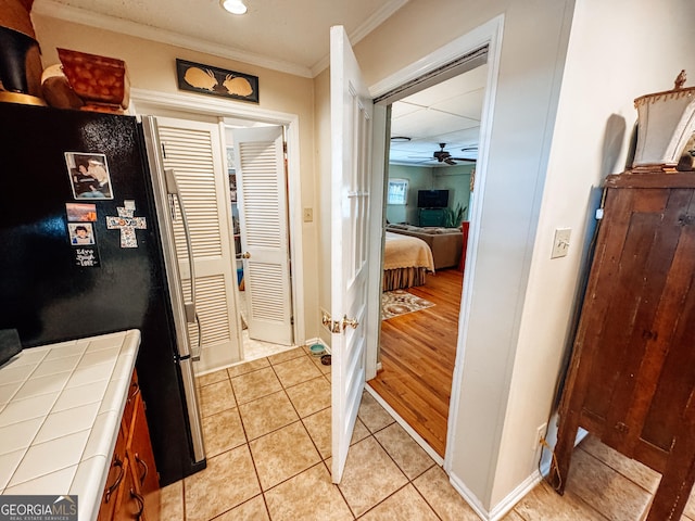 interior space featuring tile countertops, light tile patterned floors, baseboards, ornamental molding, and freestanding refrigerator