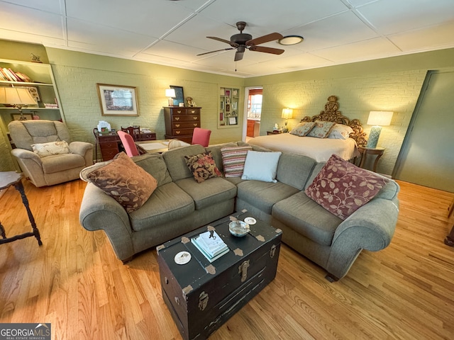 living room with brick wall, a ceiling fan, and wood finished floors