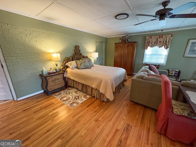 bedroom featuring ceiling fan, brick wall, light wood finished floors, and ornamental molding