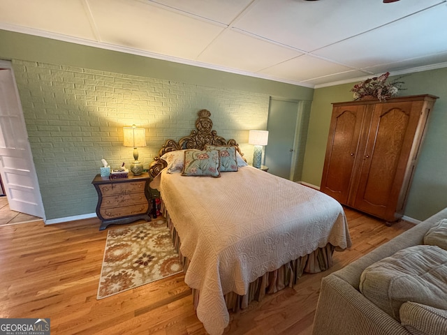 bedroom with brick wall, light wood-style flooring, and baseboards