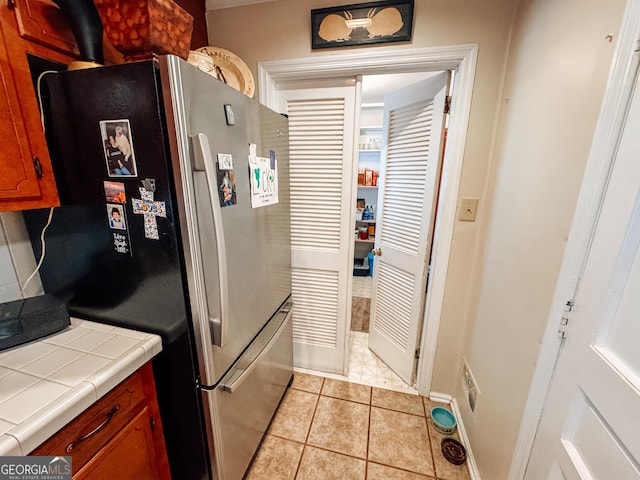 kitchen featuring tile countertops, light tile patterned flooring, brown cabinetry, and freestanding refrigerator