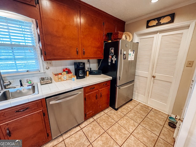 kitchen with light tile patterned floors, stainless steel appliances, tasteful backsplash, a sink, and a textured ceiling