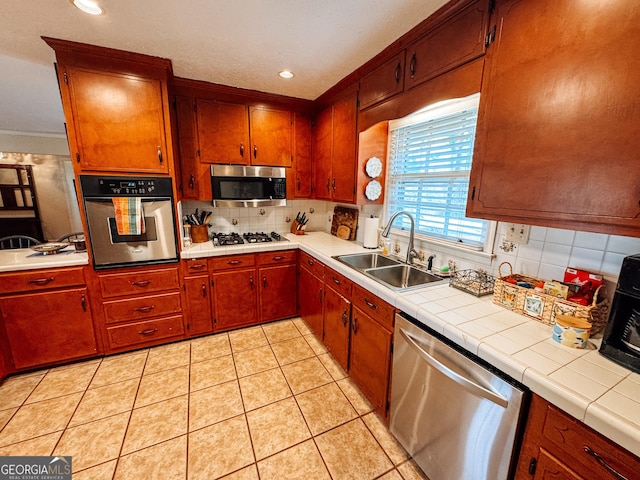 kitchen featuring tile countertops, light tile patterned flooring, a sink, appliances with stainless steel finishes, and decorative backsplash