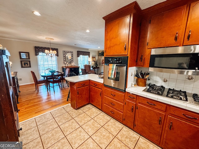 kitchen featuring brown cabinets, tasteful backsplash, appliances with stainless steel finishes, light tile patterned flooring, and a peninsula