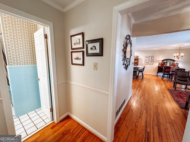 corridor featuring light wood-style floors, a wainscoted wall, a notable chandelier, and ornamental molding