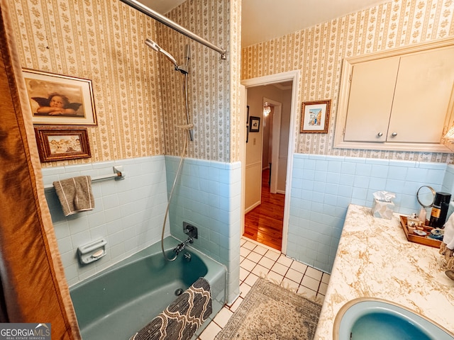 full bathroom with wallpapered walls, wainscoting, tile patterned floors, a sink, and tile walls