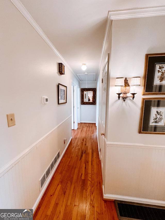 corridor featuring wood finished floors, visible vents, ornamental molding, wainscoting, and attic access