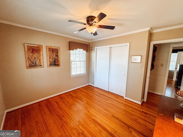 unfurnished bedroom featuring baseboards, ceiling fan, ornamental molding, wood finished floors, and a closet