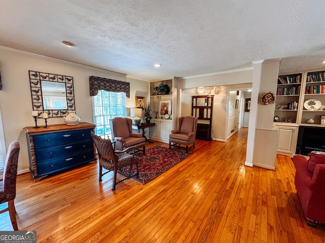 sitting room with light wood-style floors, crown molding, a textured ceiling, and baseboards