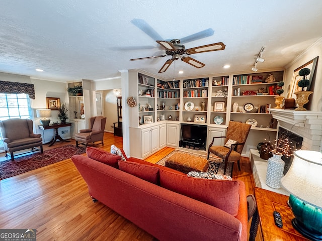 living area featuring a textured ceiling, a fireplace, wood finished floors, a ceiling fan, and crown molding