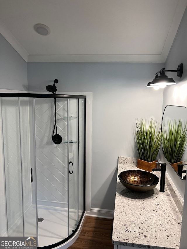 bathroom featuring a stall shower, baseboards, wood finished floors, crown molding, and vanity