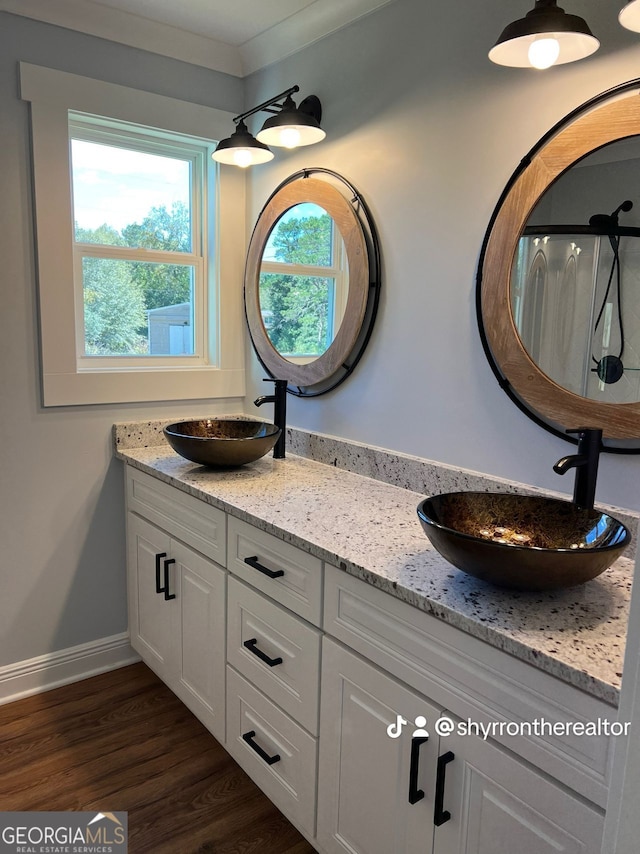 full bathroom with double vanity, wood finished floors, a sink, and baseboards