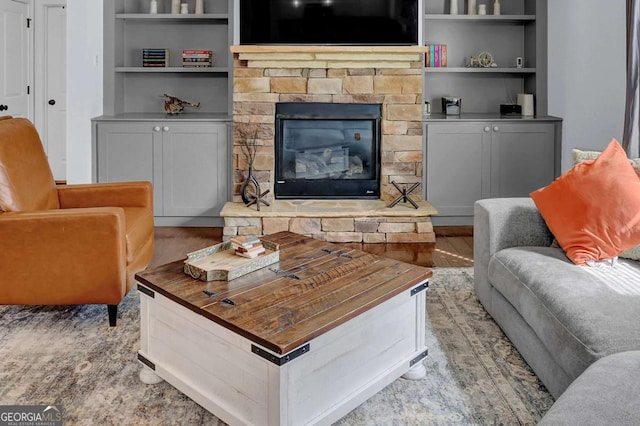 living room featuring light wood-type flooring, a fireplace, and built in features